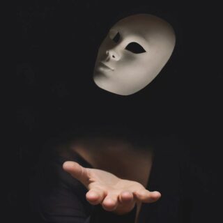 hand of a person hidden in the dark throwing a mask in the air